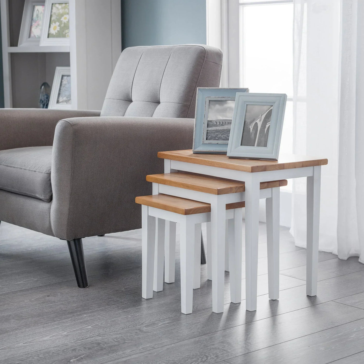 White oak nest of tables with wood tops beside grey armchair in bright living room