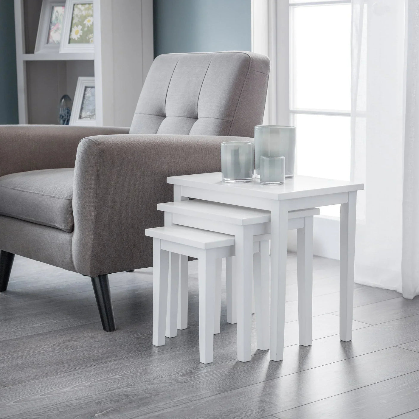 White nest of tables beside grey armchair in bright living room with candles placed on top