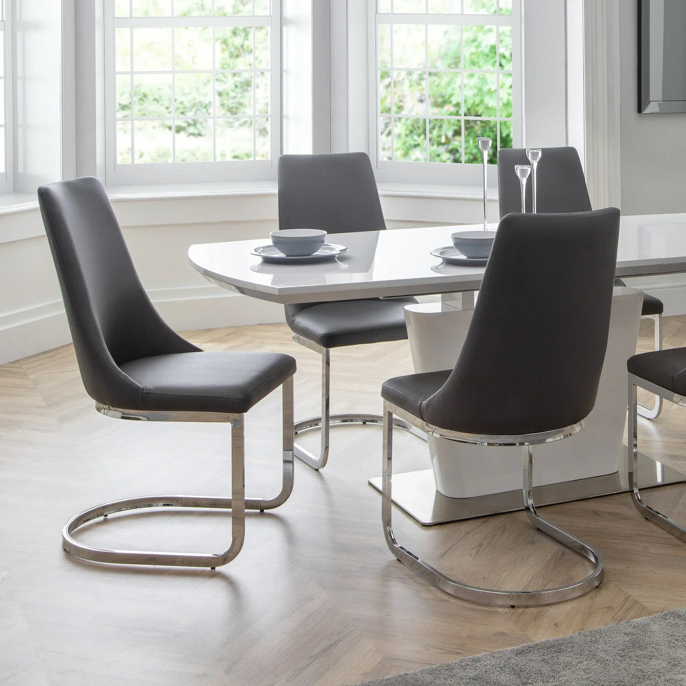 Modern dining table with six grey faux leather chairs and chrome legs in bright room