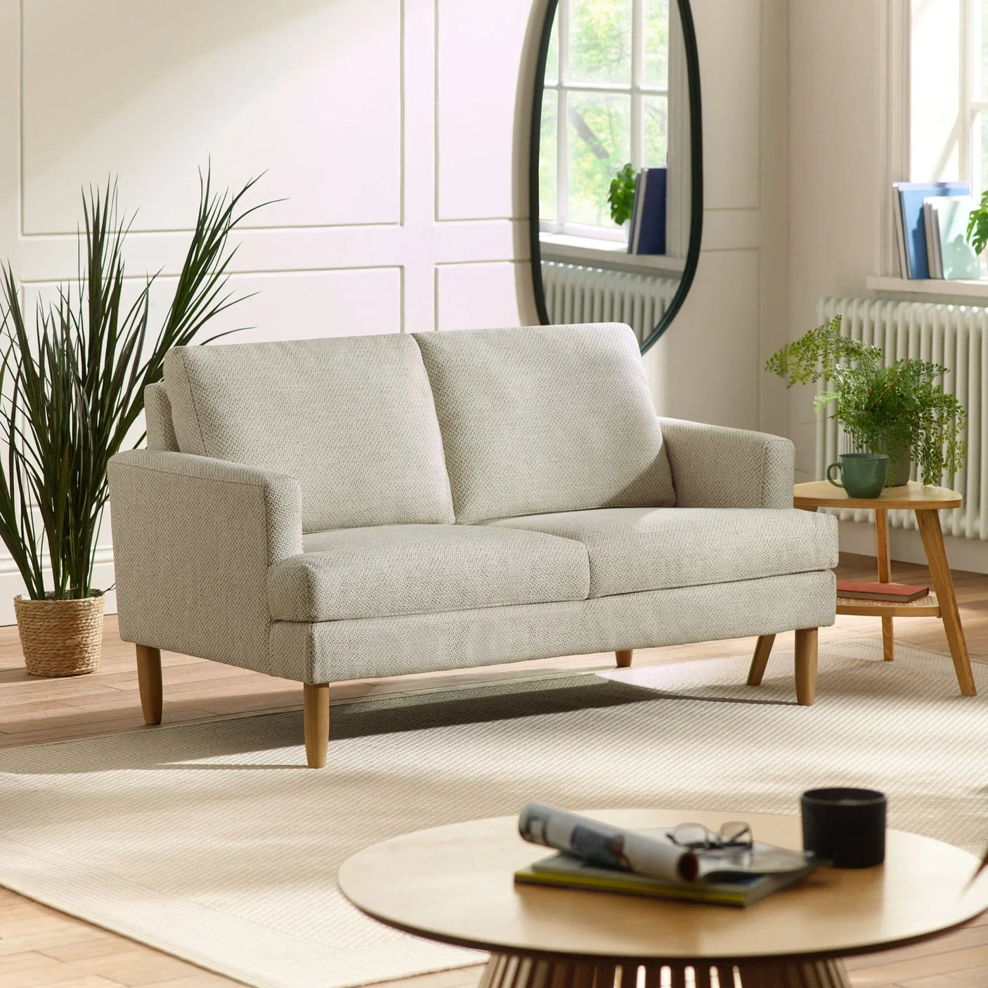 Light grey fabric sofa with wooden legs in modern living room with plants and large mirror