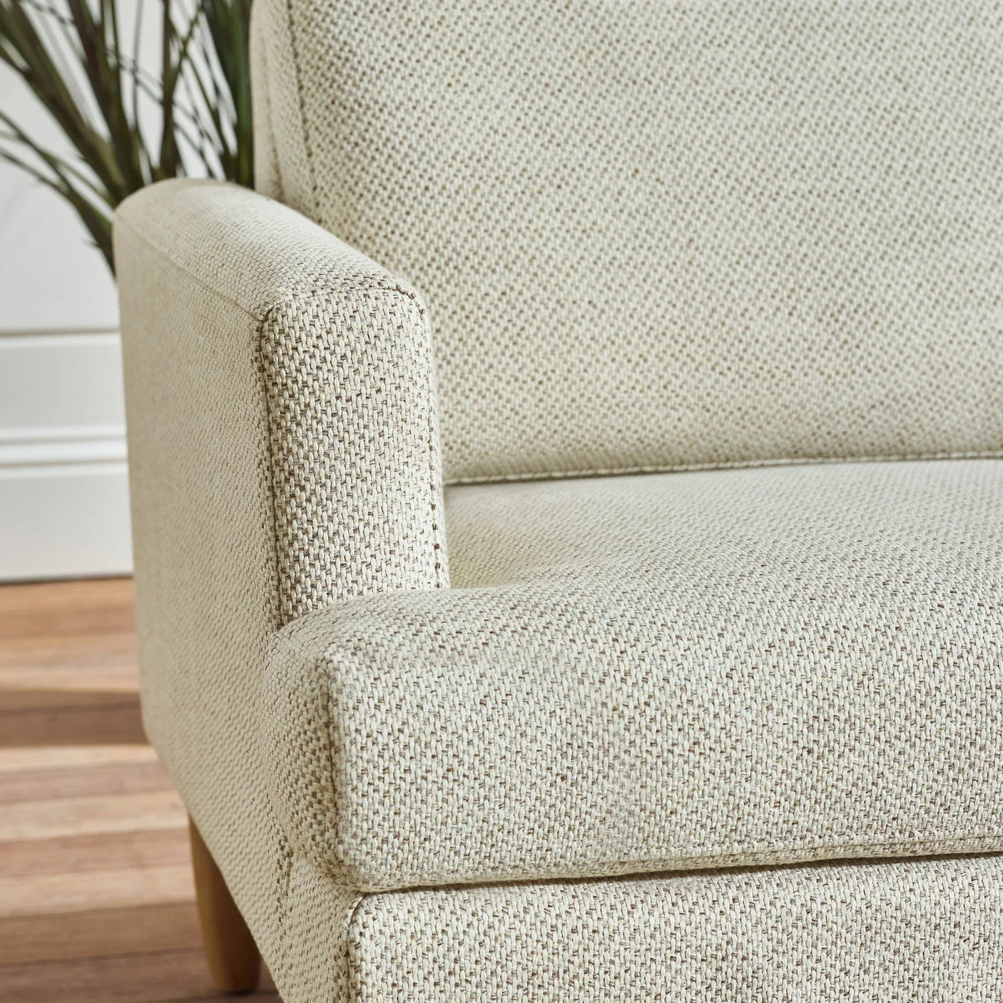 Beige fabric sofa armrest and seat closeup with textured upholstery and wooden leg