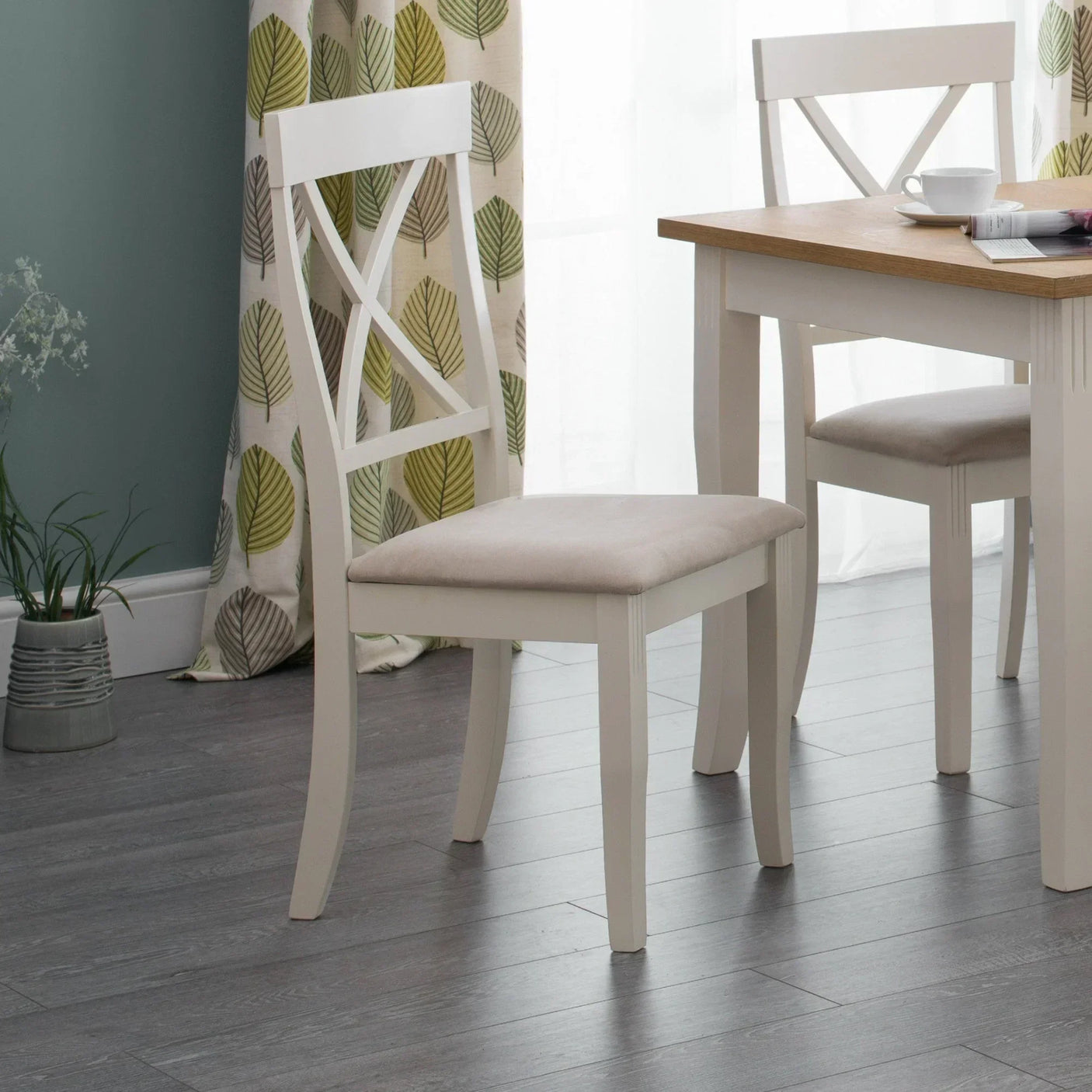 Cream dining chair with cross backrest and padded seat beside matching wood dining table