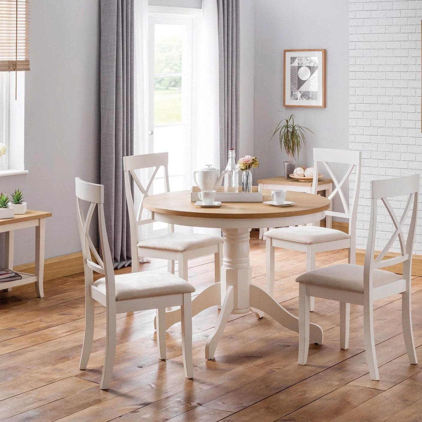 Round wood dining table with four white chairs set in a bright dining room with wooden floor