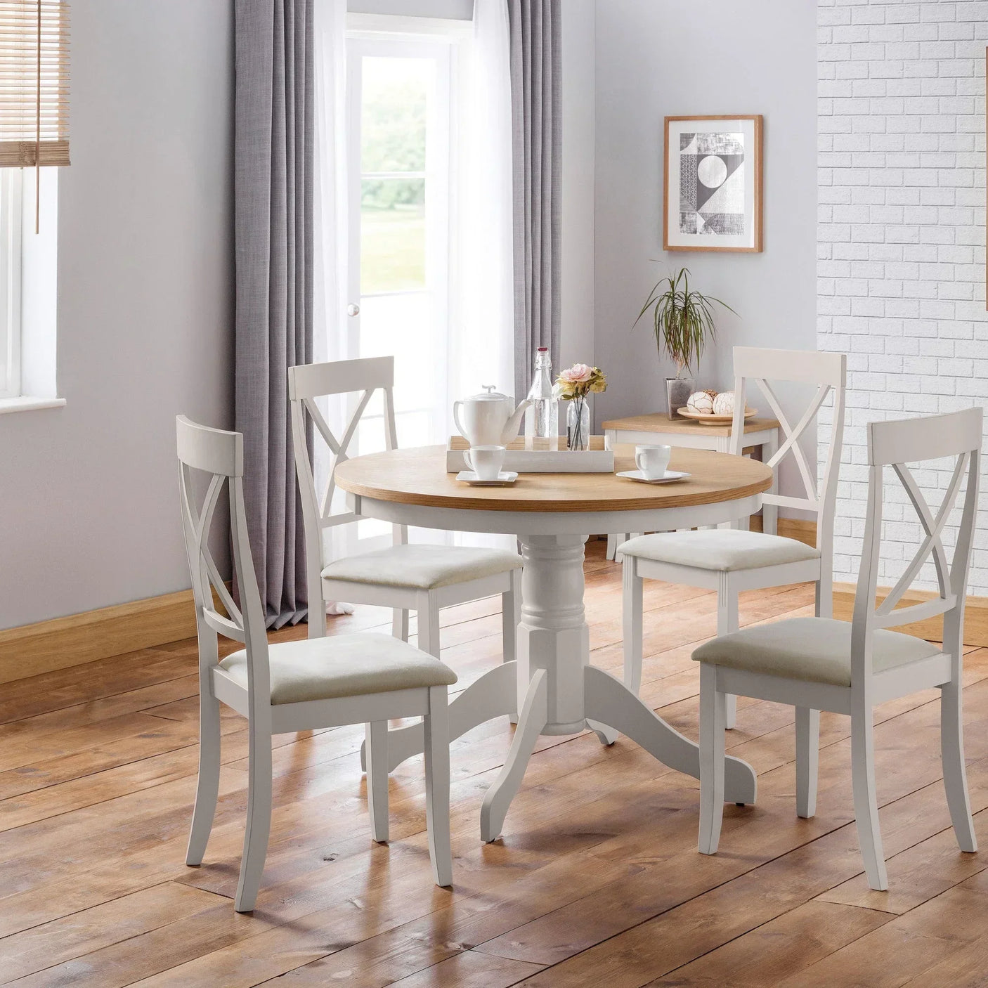 Round wooden dining table with four white chairs set on hardwood floor in bright room