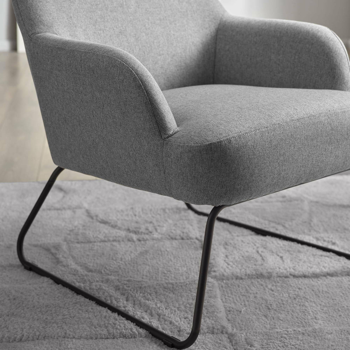 Grey fabric accent chair with curved armrests and black metal legs on light rug