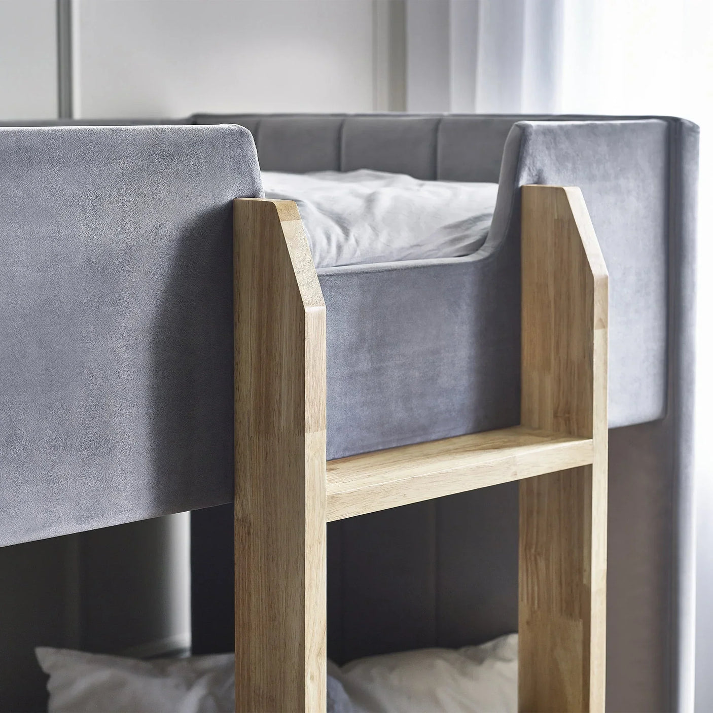 Grey fabric bunk bed with wooden ladder and soft upholstered panels in a bright bedroom