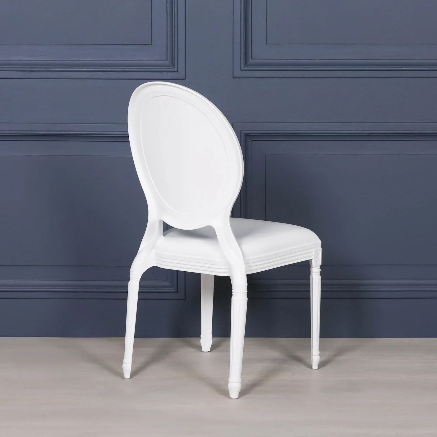 White dining chair with oval back and tapered legs against a dark blue wall