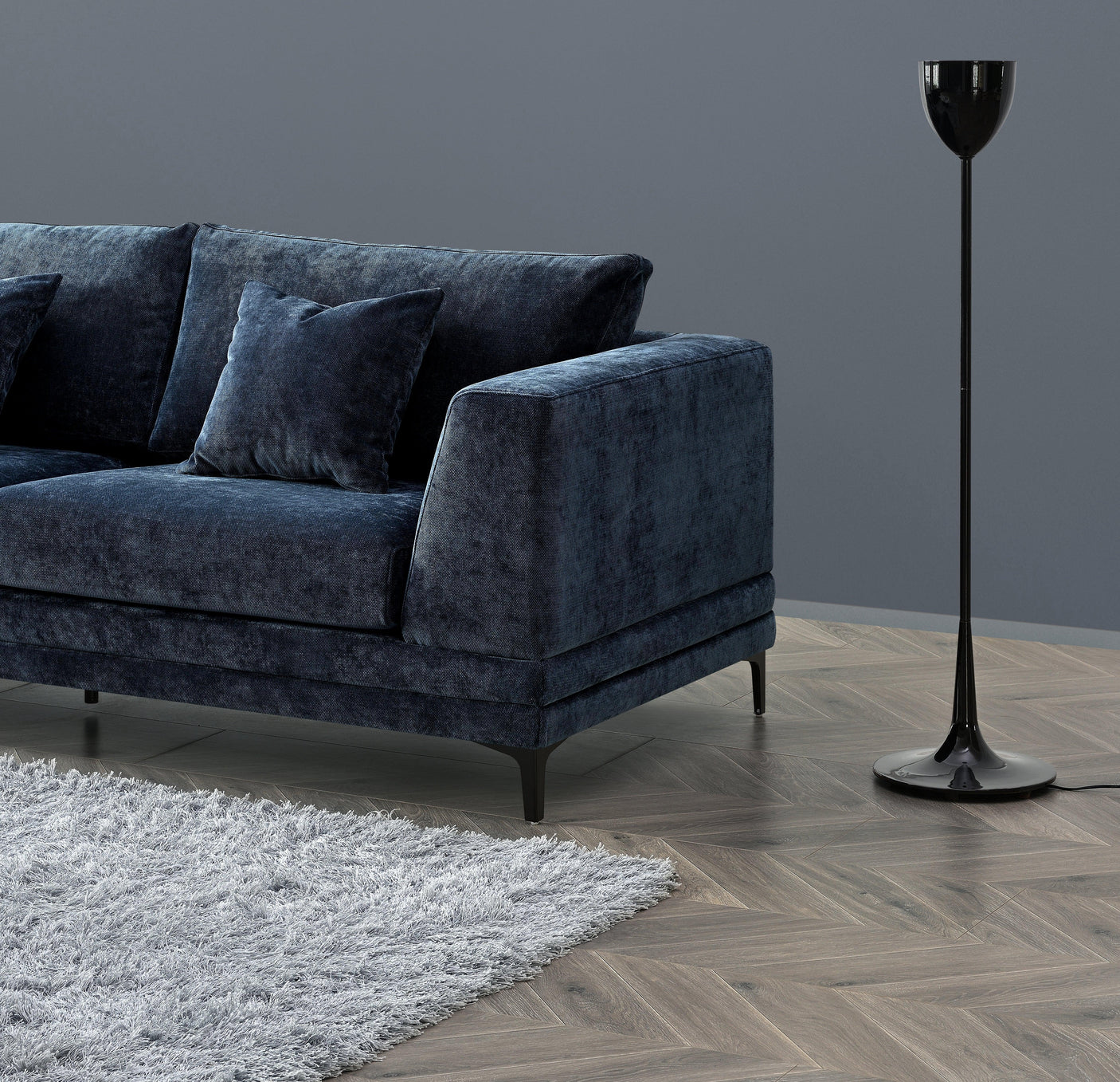 Dark blue velvet sofa with matching cushions beside modern black floor lamp on wooden herringbone floor