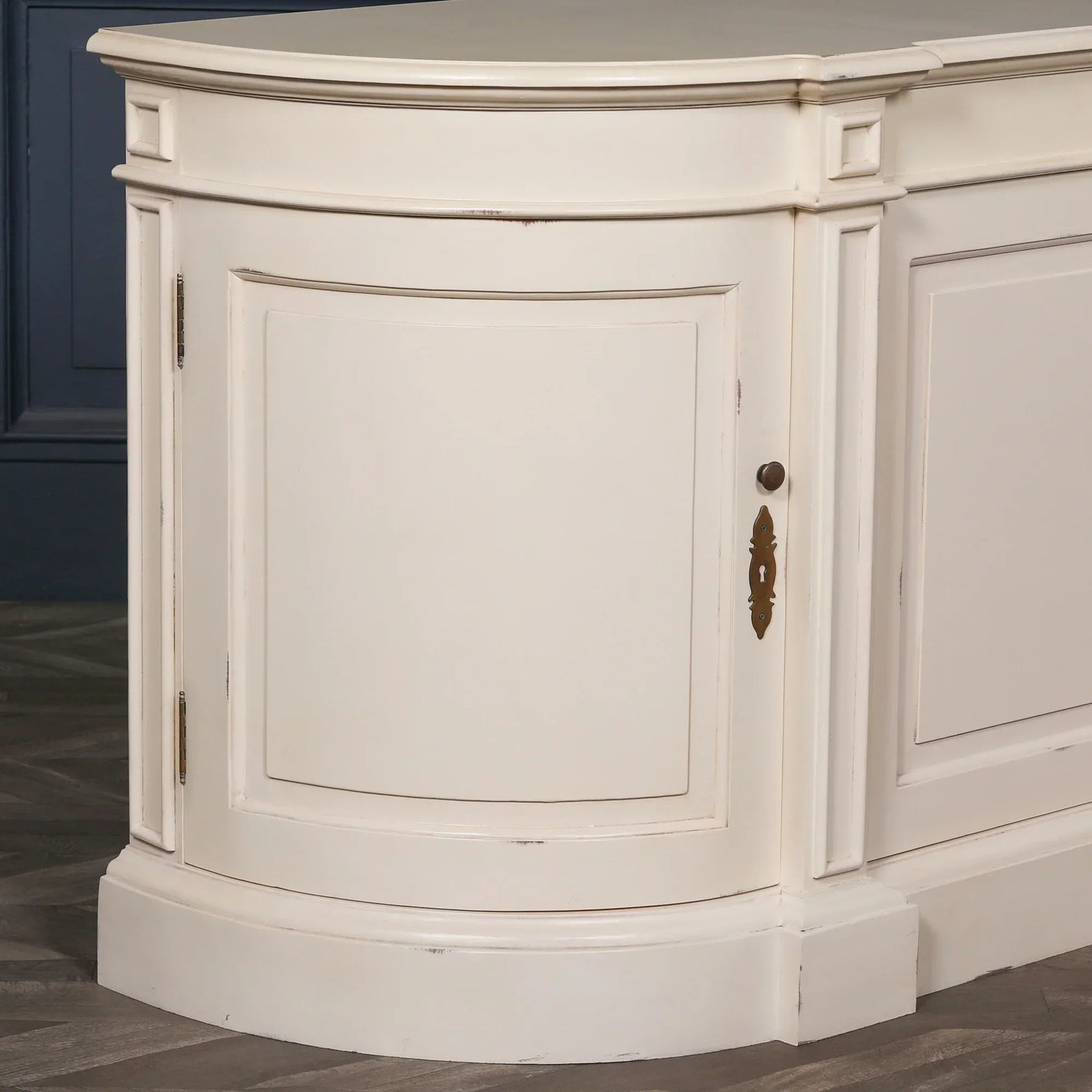 Cream painted wood sideboard cabinet corner with curved door and brass keyhole detail