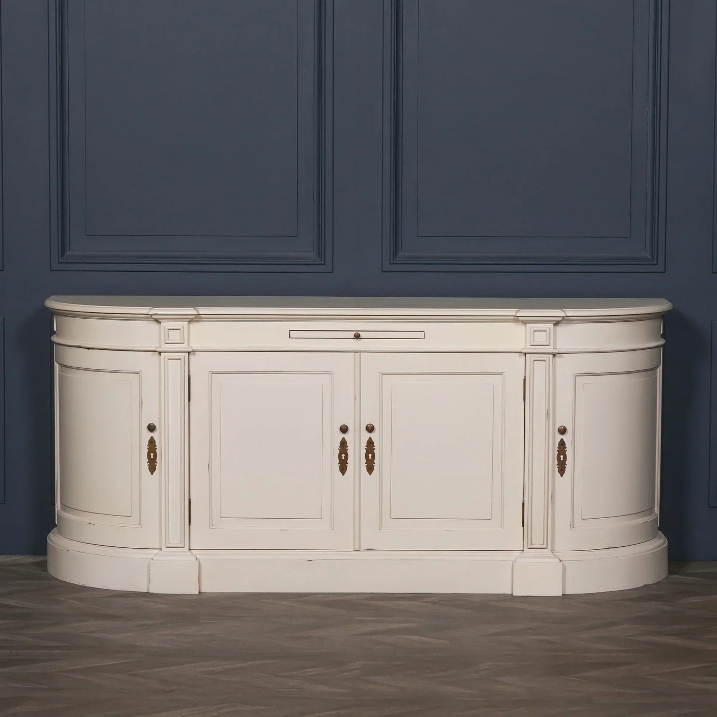 Cream sideboard cabinet with curved ends and brass handles against navy paneled wall