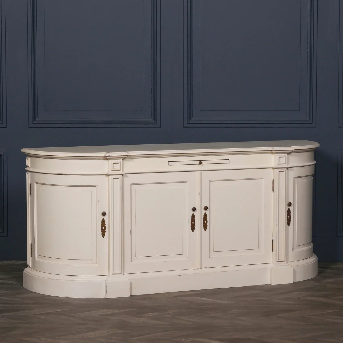 Cream painted sideboard cabinet with curved ends and brass handles against a blue wall