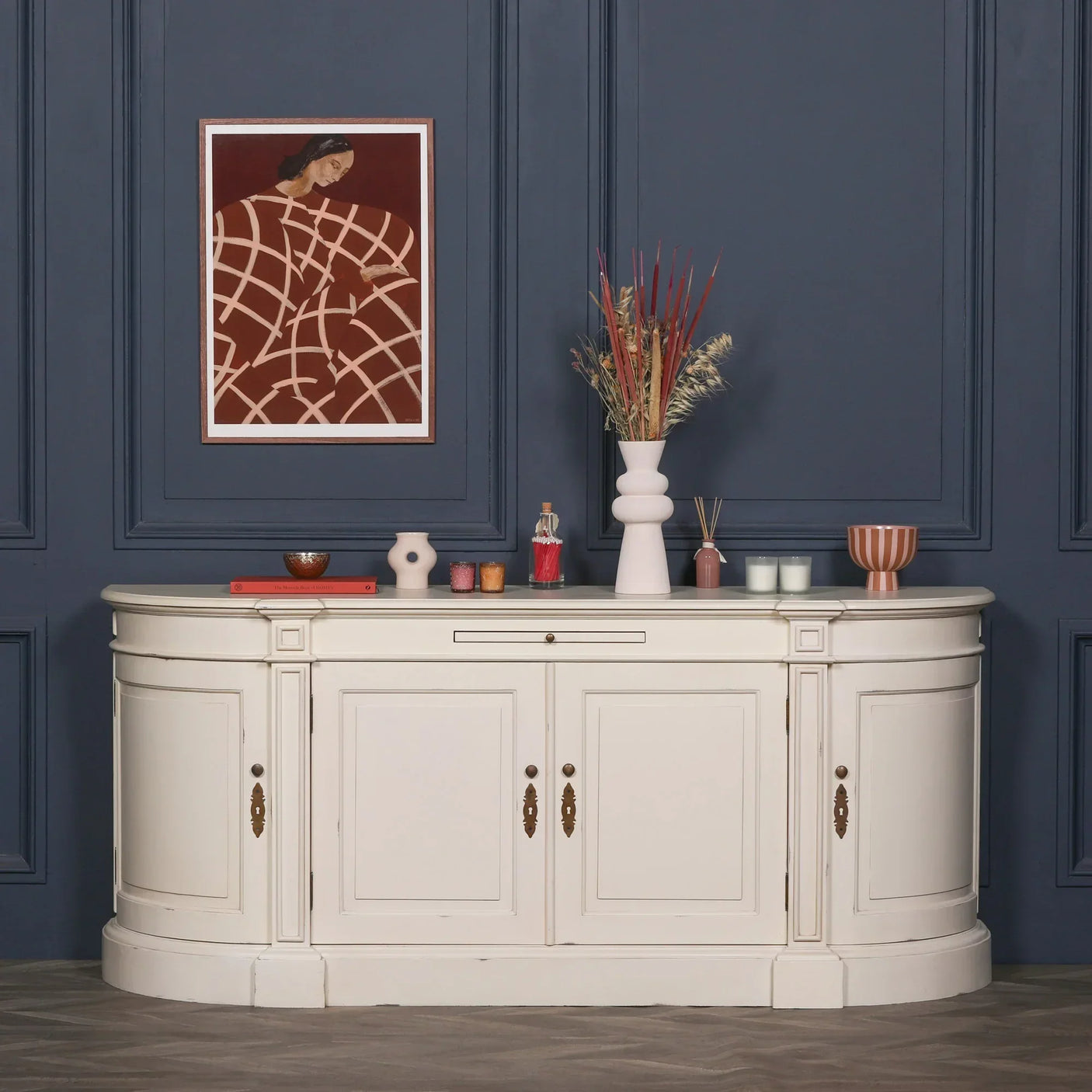 White sideboard cabinet with brass handles against navy wall, decorated with vases and candles