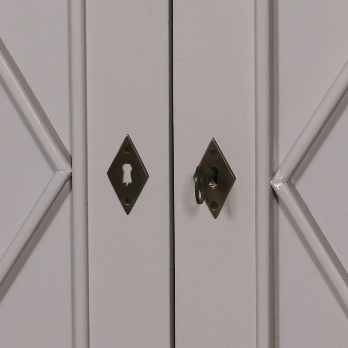 Closeup of cabinet doors with brass diamond keyhole plates and a decorative wooden panel