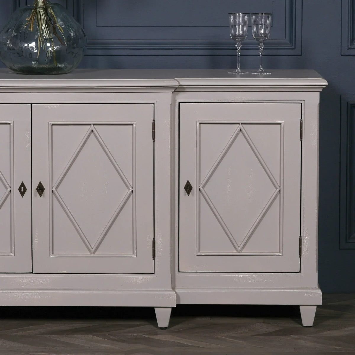 Grey sideboard with diamond panel doors, glass vase and glasses on top, against blue wall