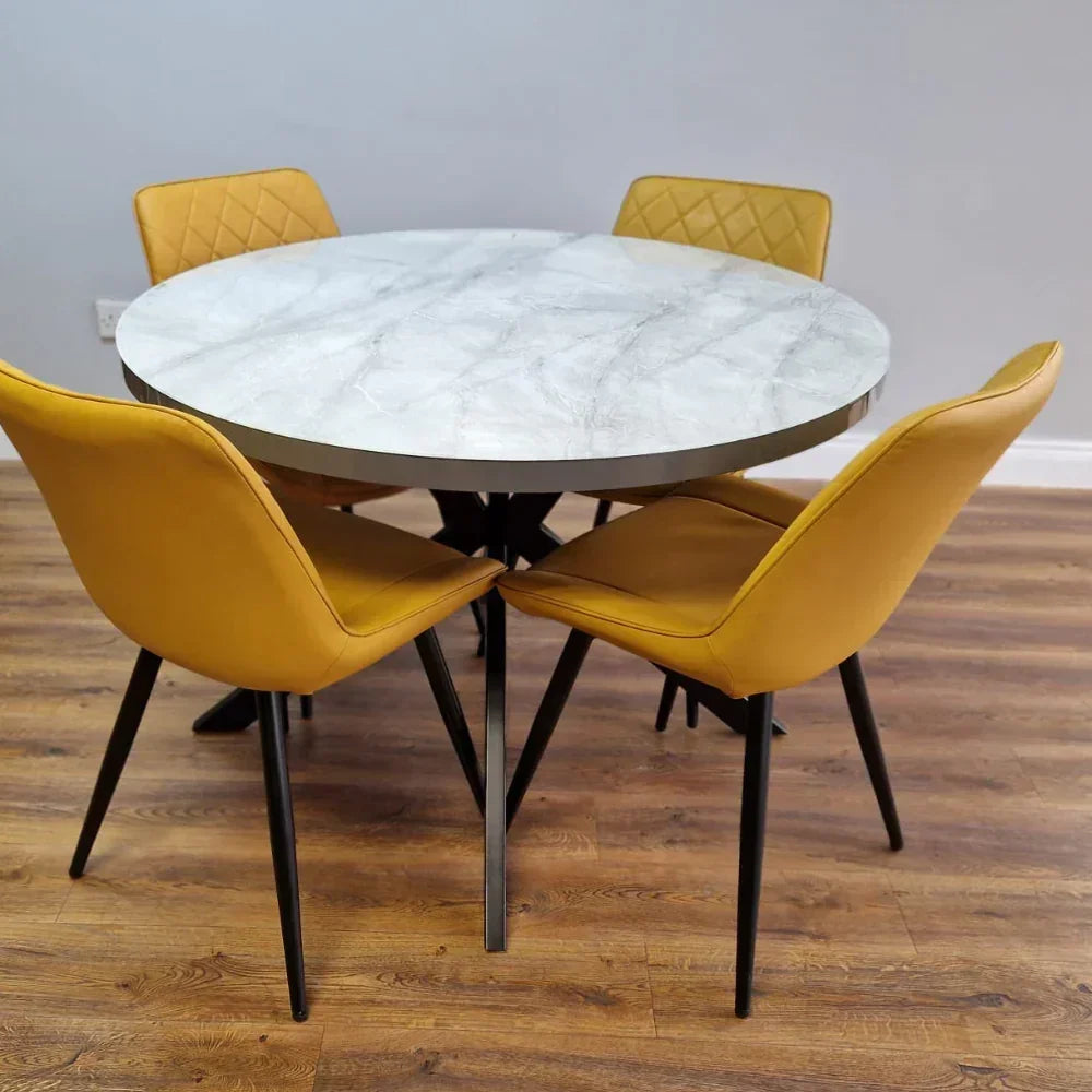 Round dining table with marble-effect top, black X legs, and mustard chairs on wooden floor