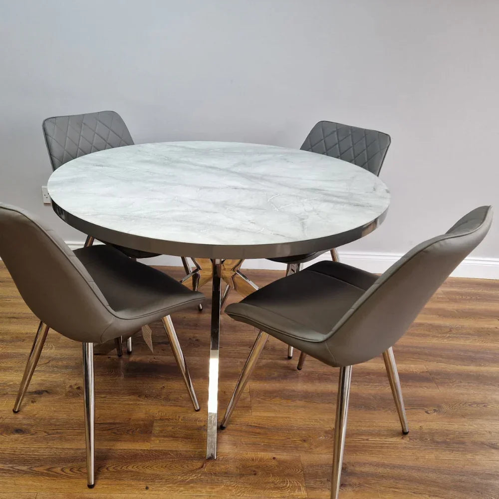 Round marble dining table with chrome legs and four grey quilted chairs on wood floor