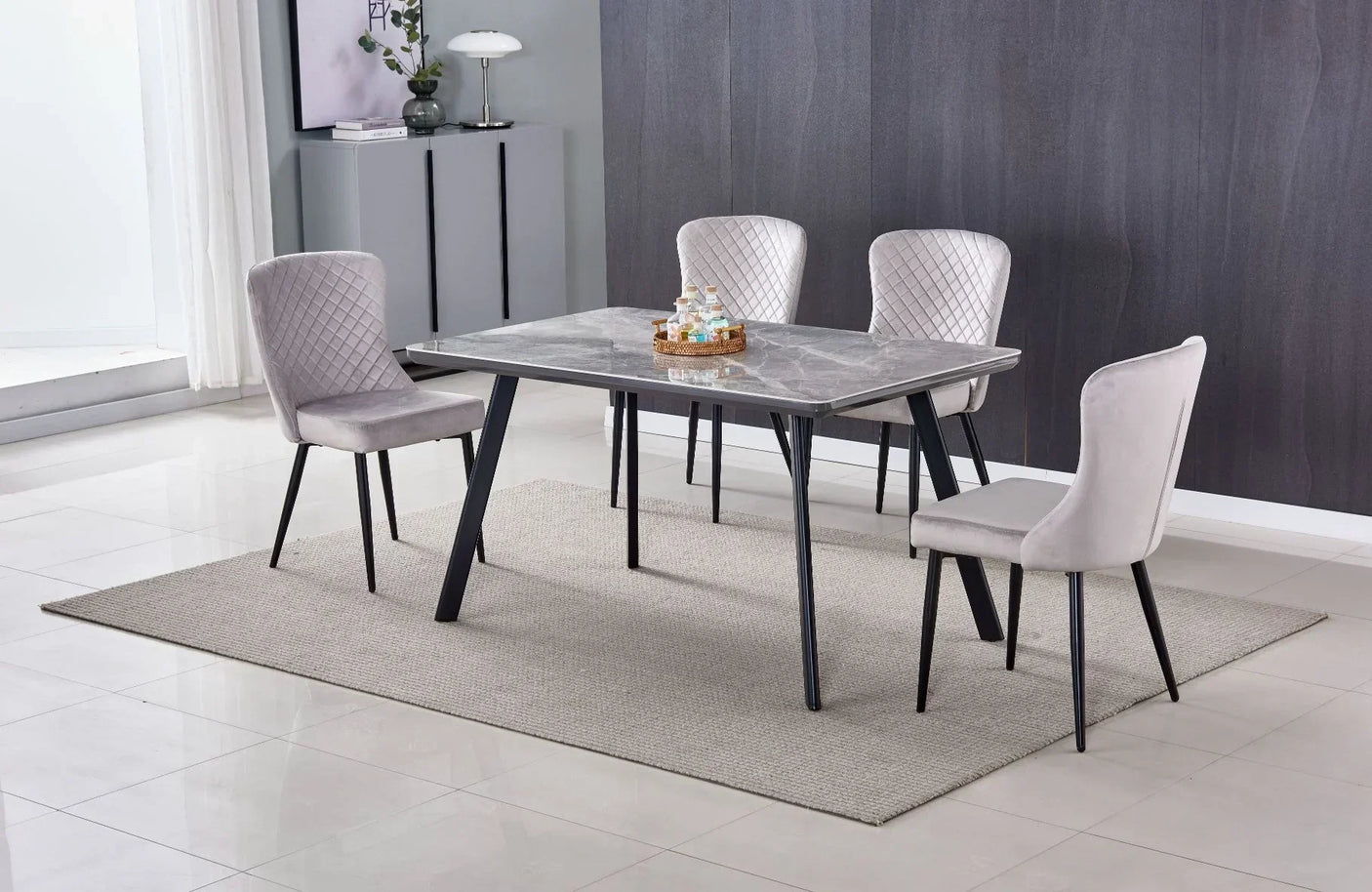 Marble-effect dining table with black legs and four grey velvet chairs on a beige rug