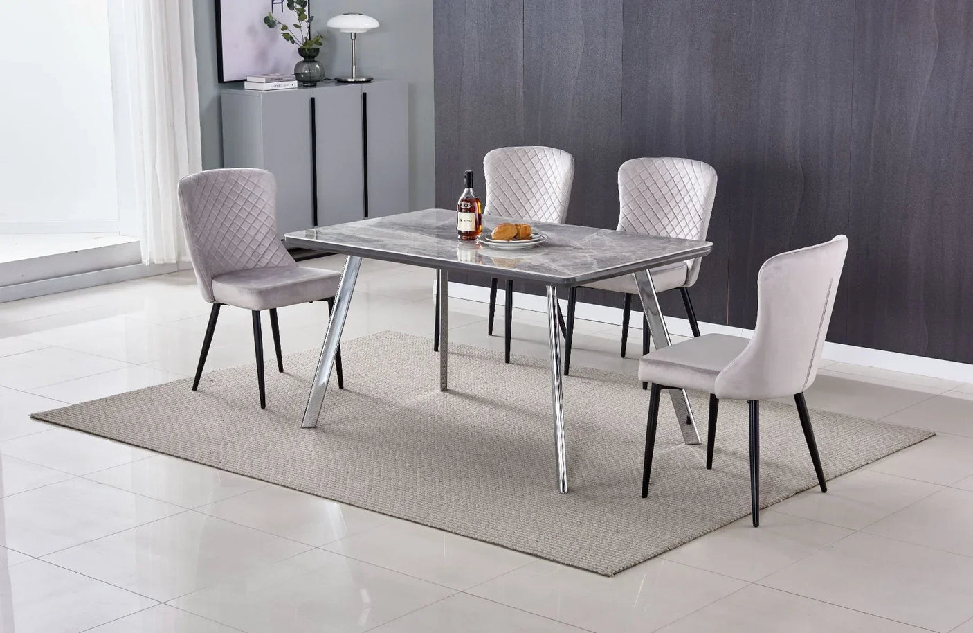 Marble dining table with chrome legs and four grey upholstered chairs on a beige rug
