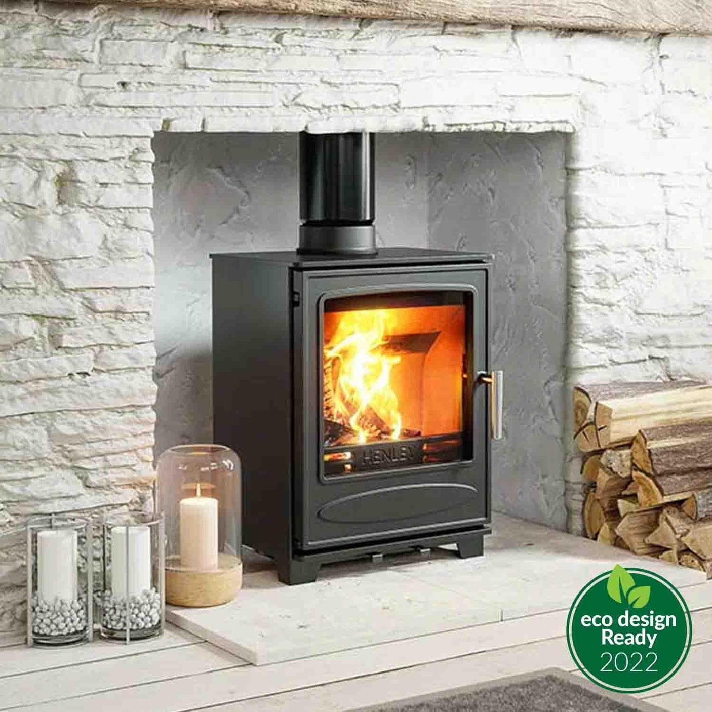 Black wood burning stove in stone fireplace, logs and candles on hearth, eco design badge