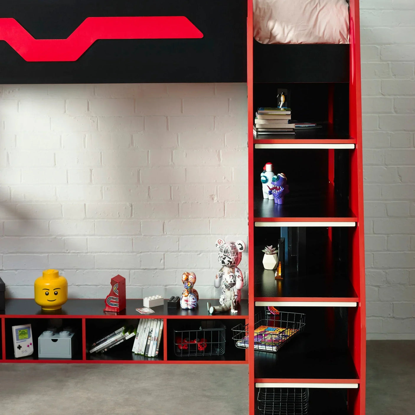Red and black bunk bed with storage shelves and desk against white brick wall