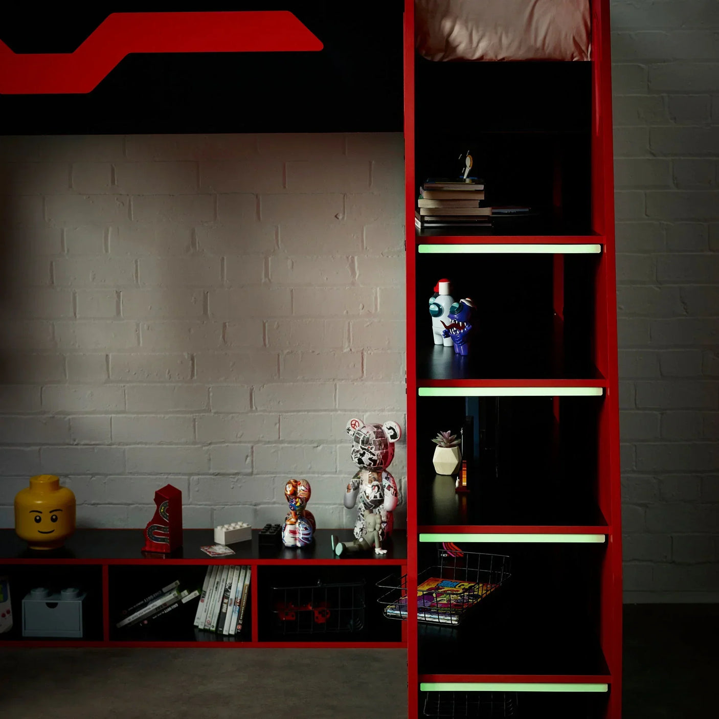 Red and black bunk bed with integrated shelving, toys, and books against a brick wall