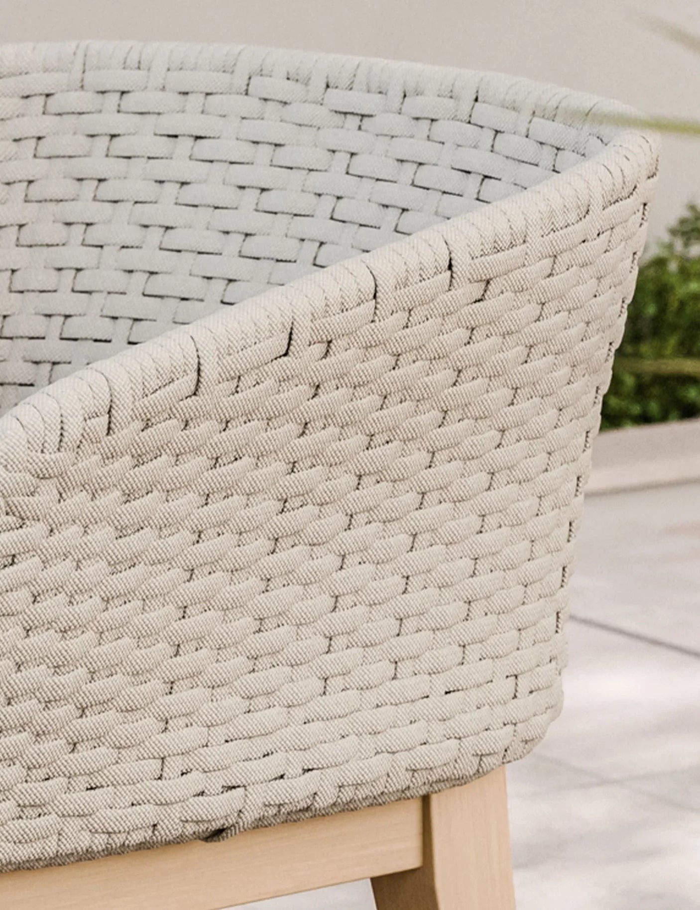Beige woven armchair with wooden legs on outdoor patio