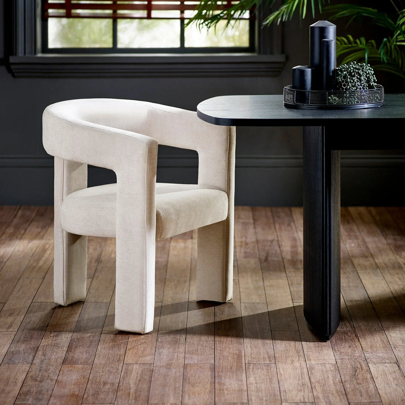 Modern cream fabric dining chair with curved backrest next to black table on wood floor