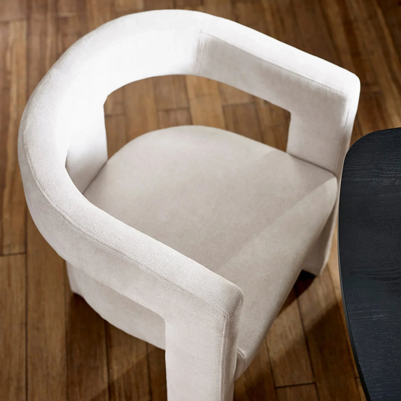 Cream upholstered accent chair with curved backrest on wooden floor beside black table
