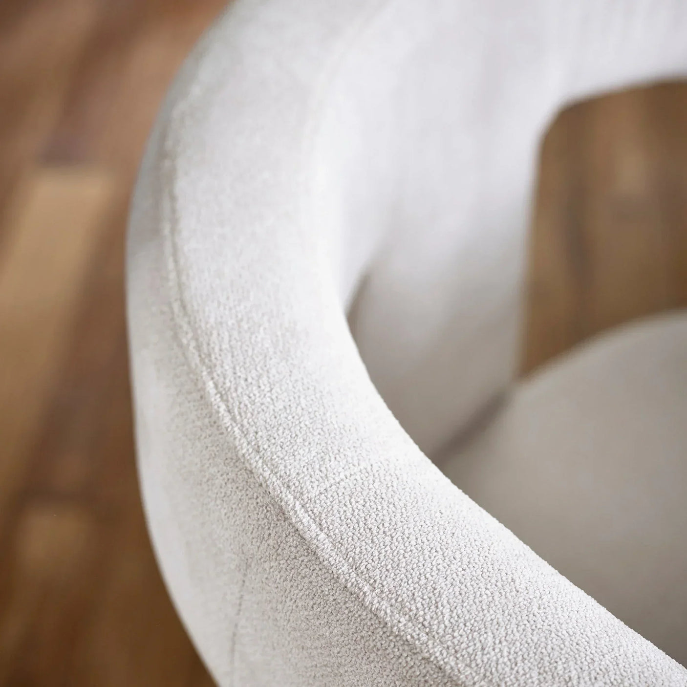 Curved boucle accent chair backrest in cream fabric on wooden floor