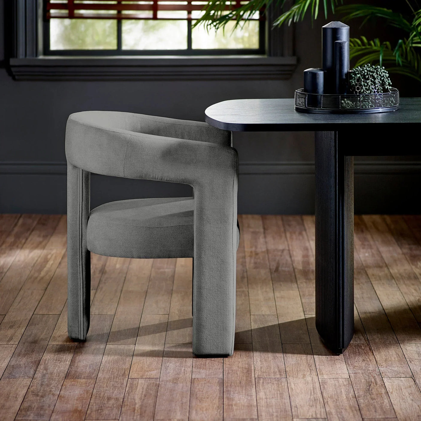 Modern grey dining chair with curved backrest at dark wood dining table on wooden floor