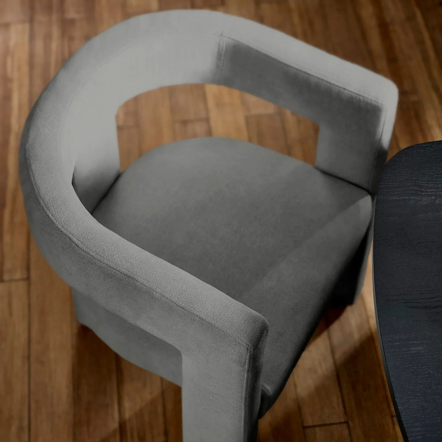 Grey fabric dining chair with curved backrest next to dark wood table on hardwood floor