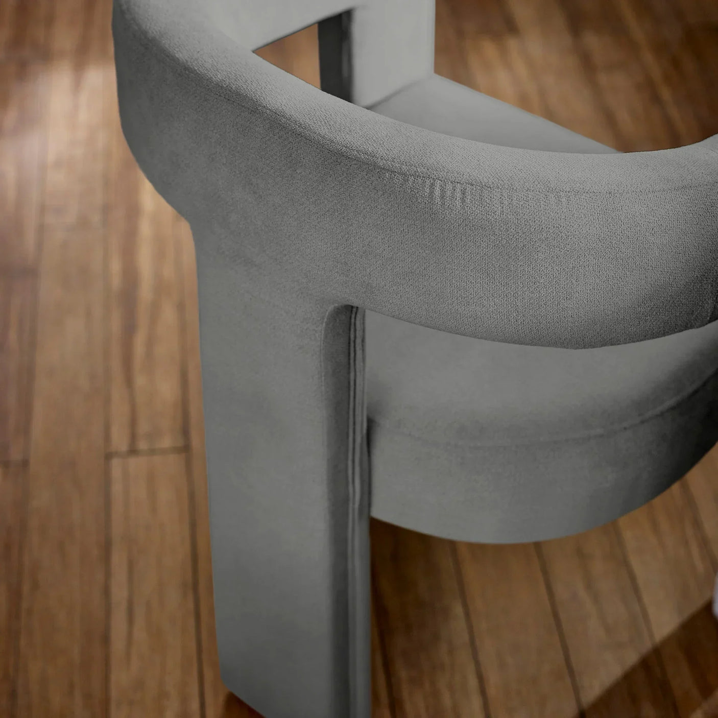 Grey velvet accent chair curved backrest on wooden floor close-up