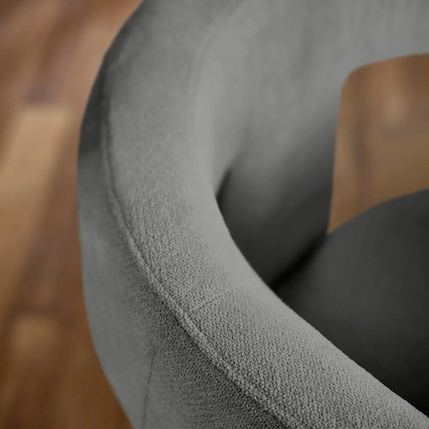 Close detail of grey boucle fabric armrest on modern dining chair with wooden floor background