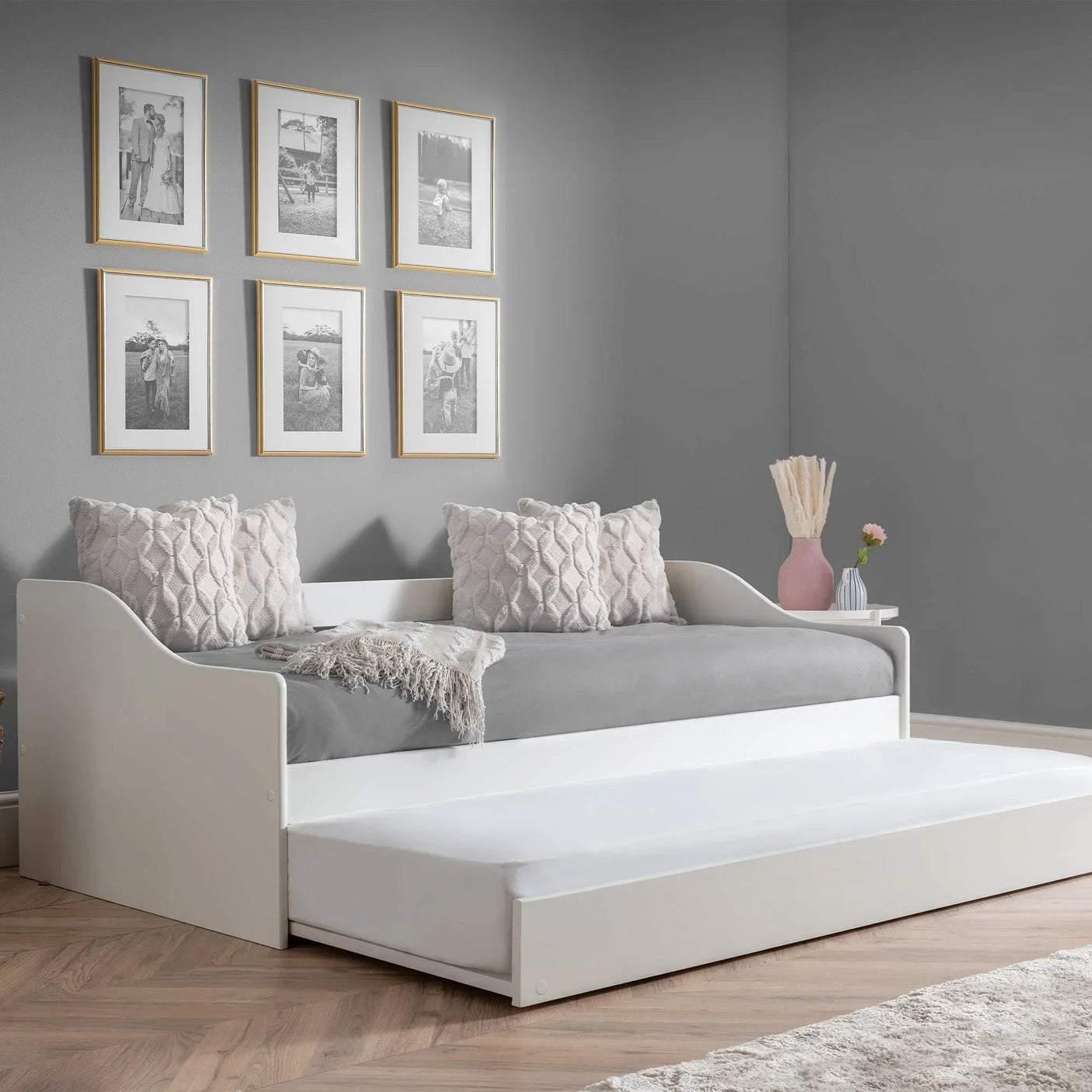 White single daybed with pull-out trundle in modern grey room, two textured cushions, wall art