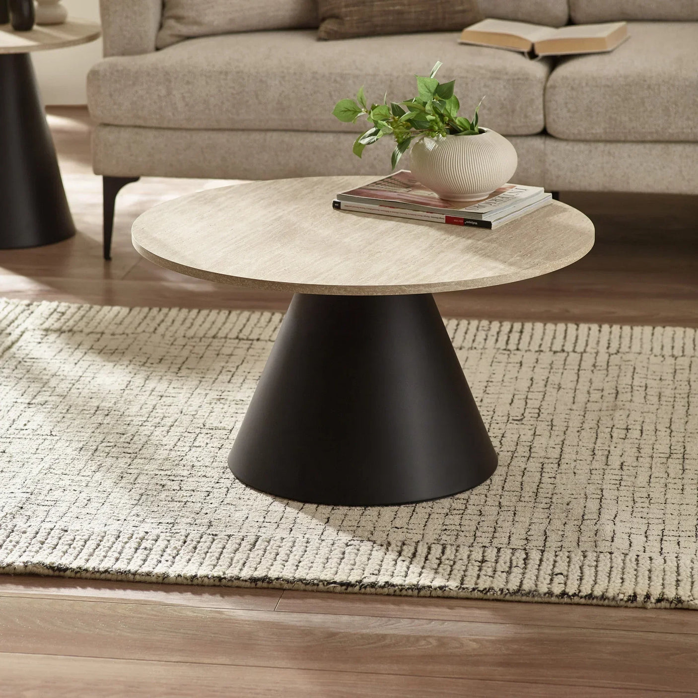 Round coffee table with light wood top, black base, and plant decor on textured rug