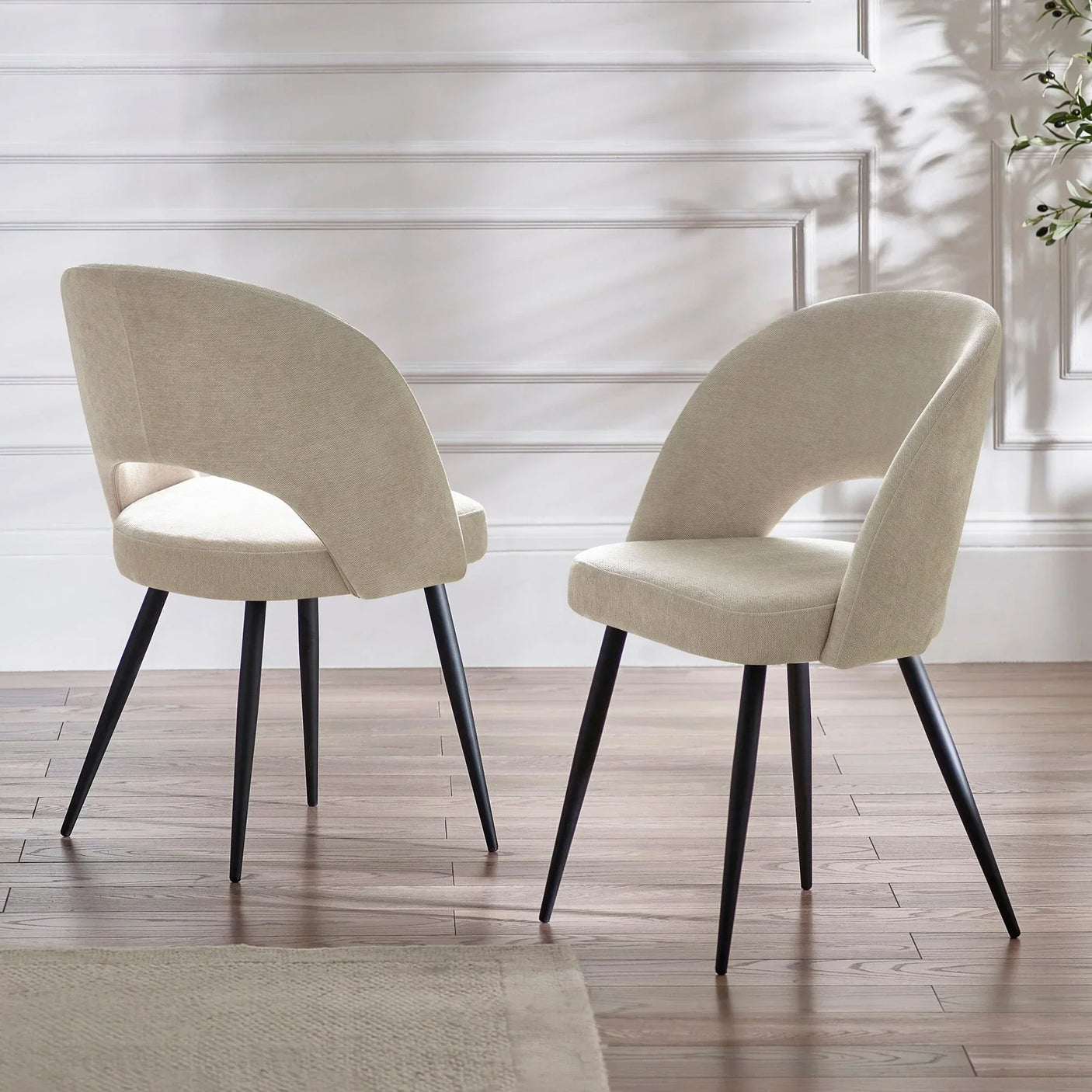 Pair of beige fabric dining chairs with black legs on wooden floor