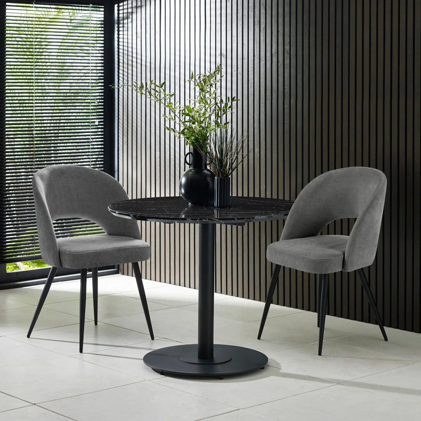 Round black dining table with marble top and two grey velvet chairs in modern room