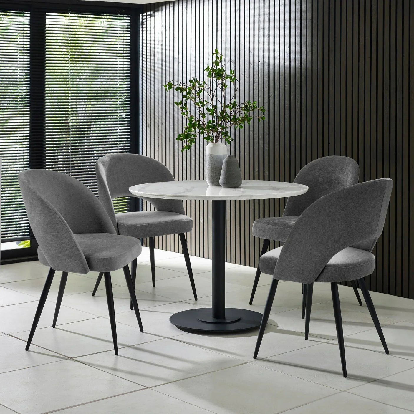 Round marble dining table with black base and four grey velvet chairs in modern dining room