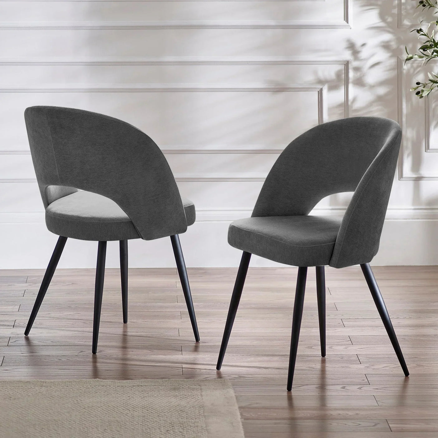 Pair of grey upholstered dining chairs with curved backs and black legs on wooden floor