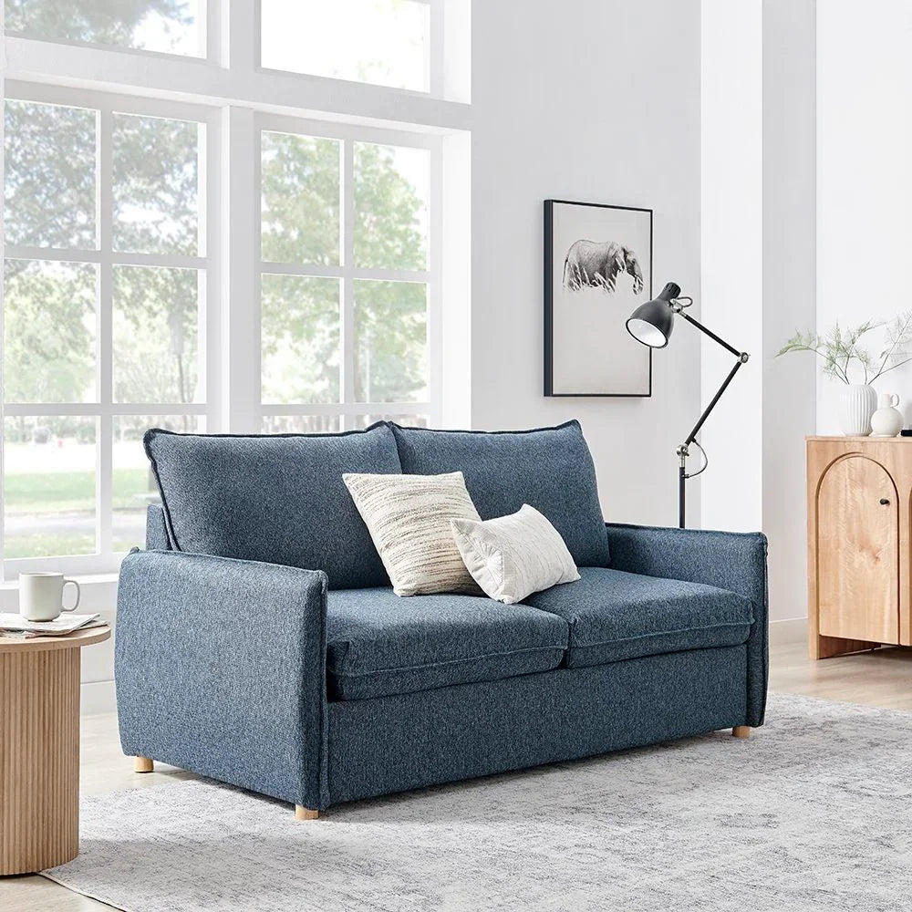 Blue fabric two-seater sofa with cushions in bright living room with large window