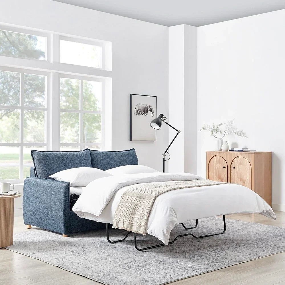 Blue fabric sofa bed extended with white bedding in modern living room