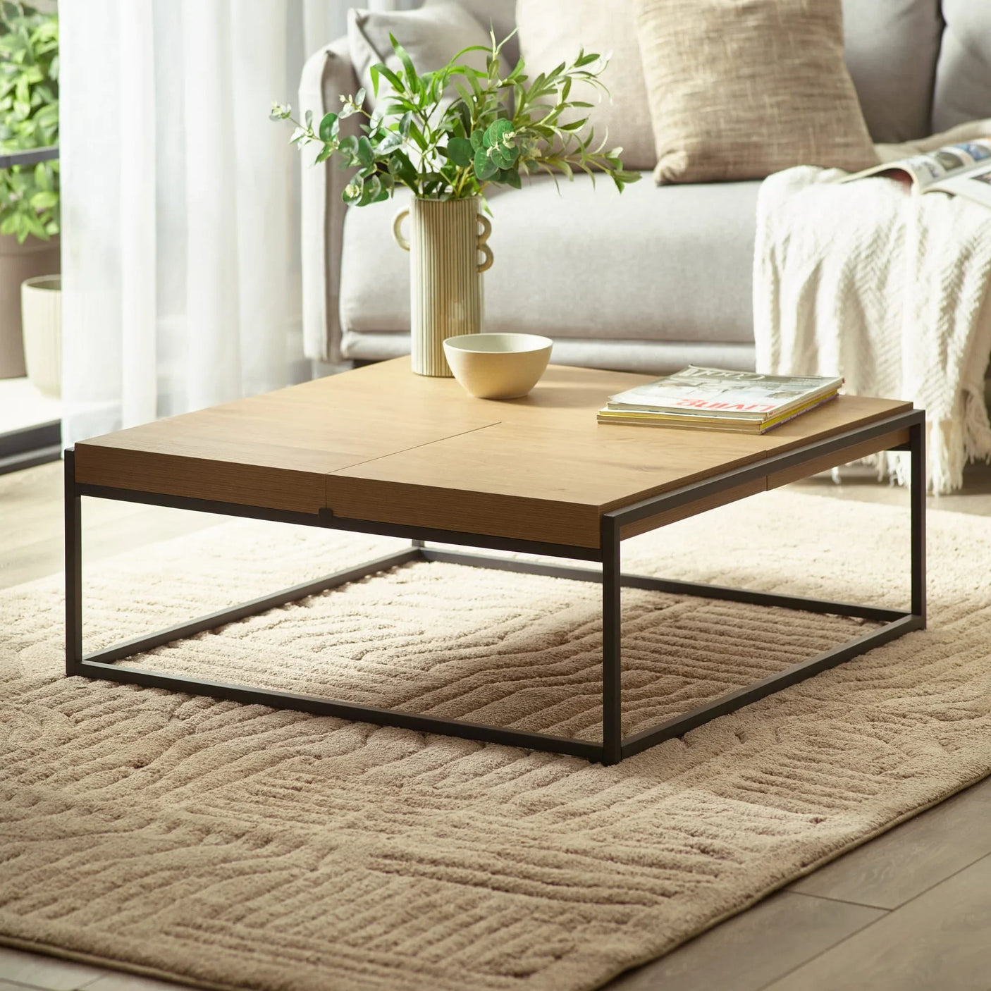 Wooden coffee table with black metal frame on beige rug, decor and magazines on top