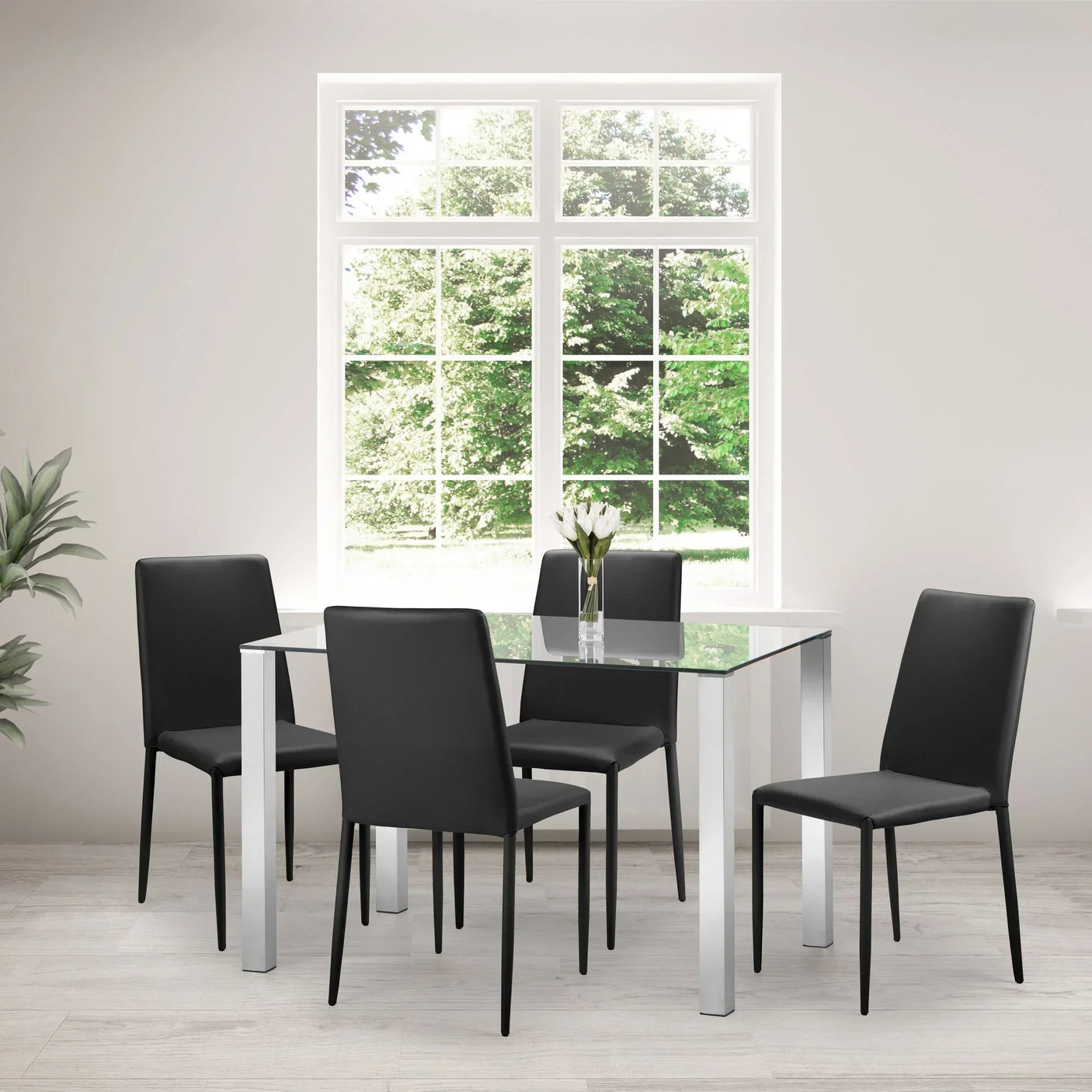 Glass dining table with chrome legs and four black chairs in modern dining room setting