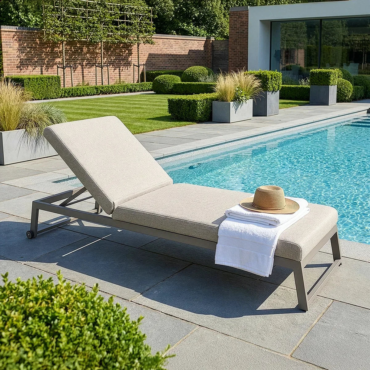 Aluminium sun lounger with beige cushion beside pool, towel and hat placed on seat