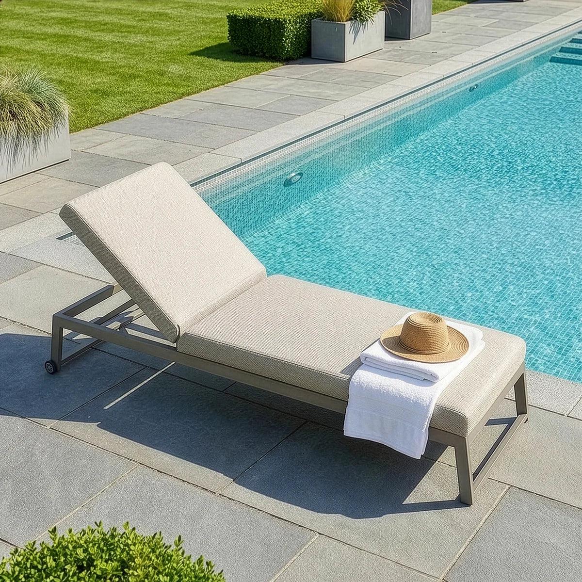 Aluminium sun lounger with beige cushion by swimming pool, towel and hat on seat