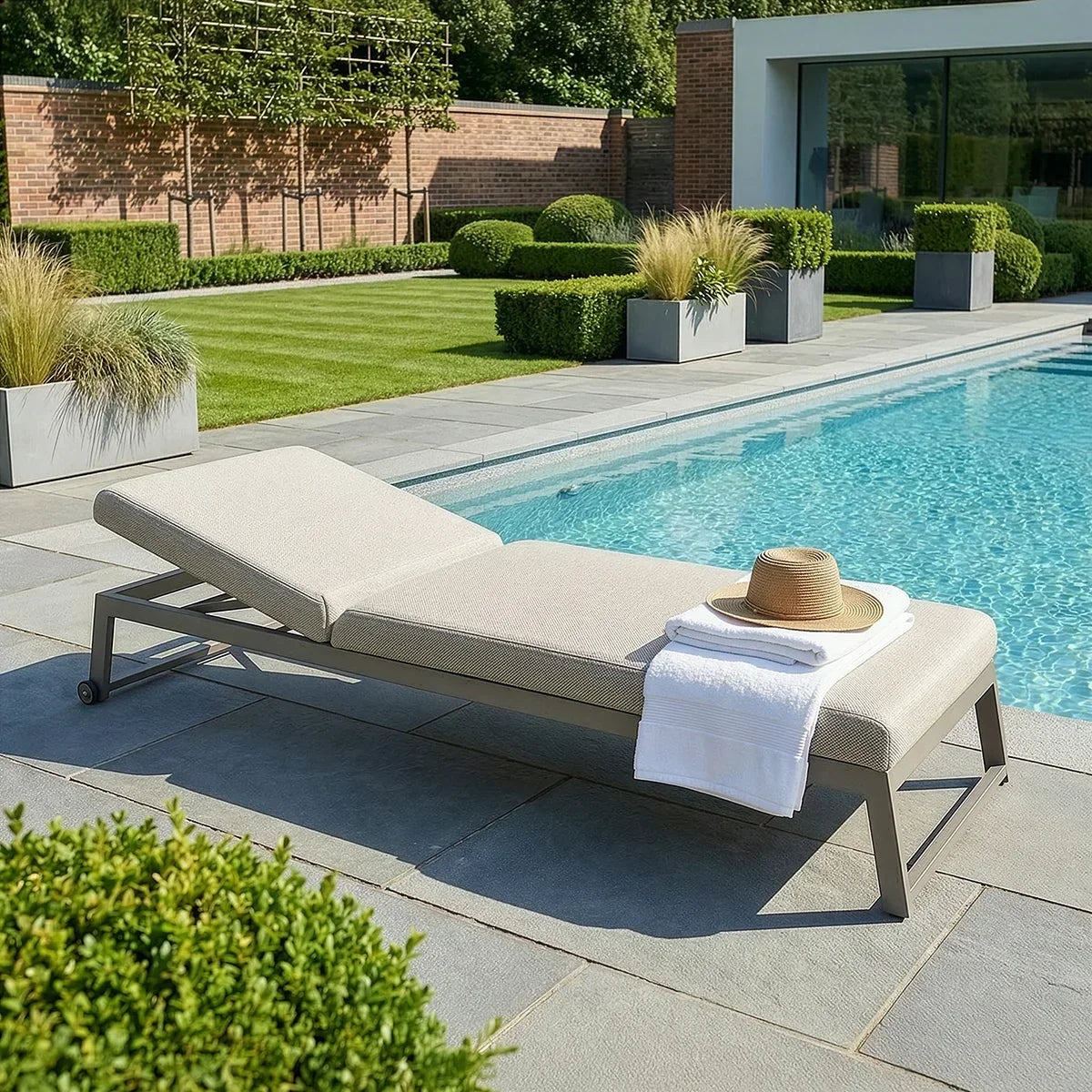 Aluminium sun lounger with beige cushion beside pool, towel and hat on seat