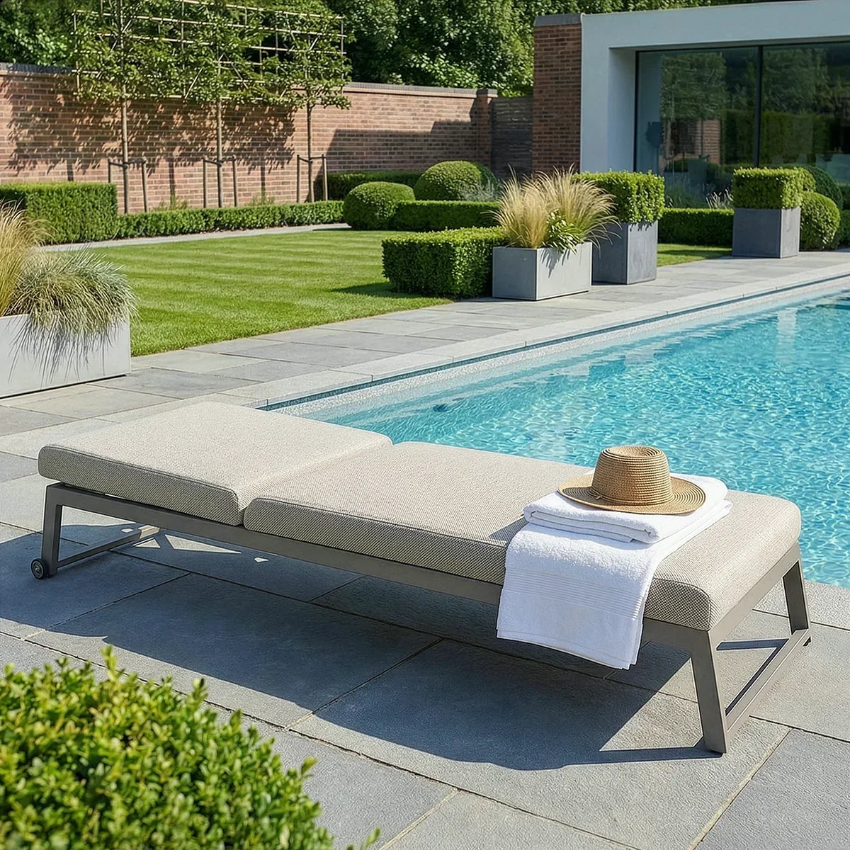 Aluminium sun lounger with beige cushion by poolside, towel and sun hat on seat