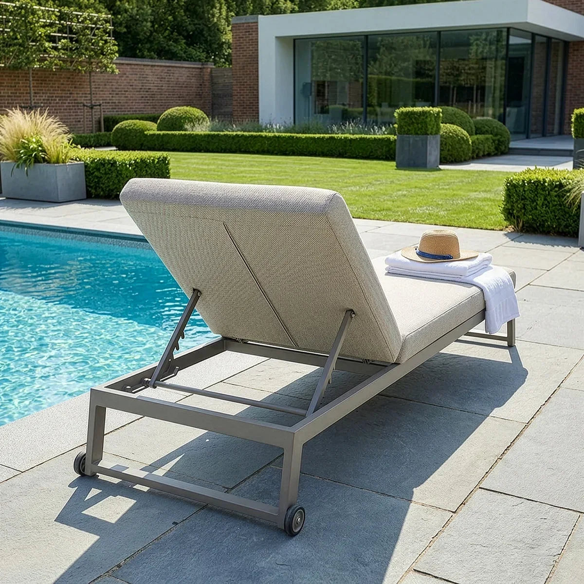 aluminium sun lounger with beige cushion beside pool, towel and hat on seat
