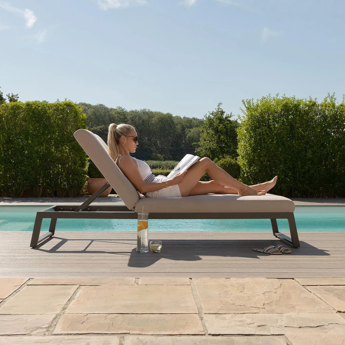 Aluminium sun lounger with beige cushion by poolside, woman relaxing outdoors