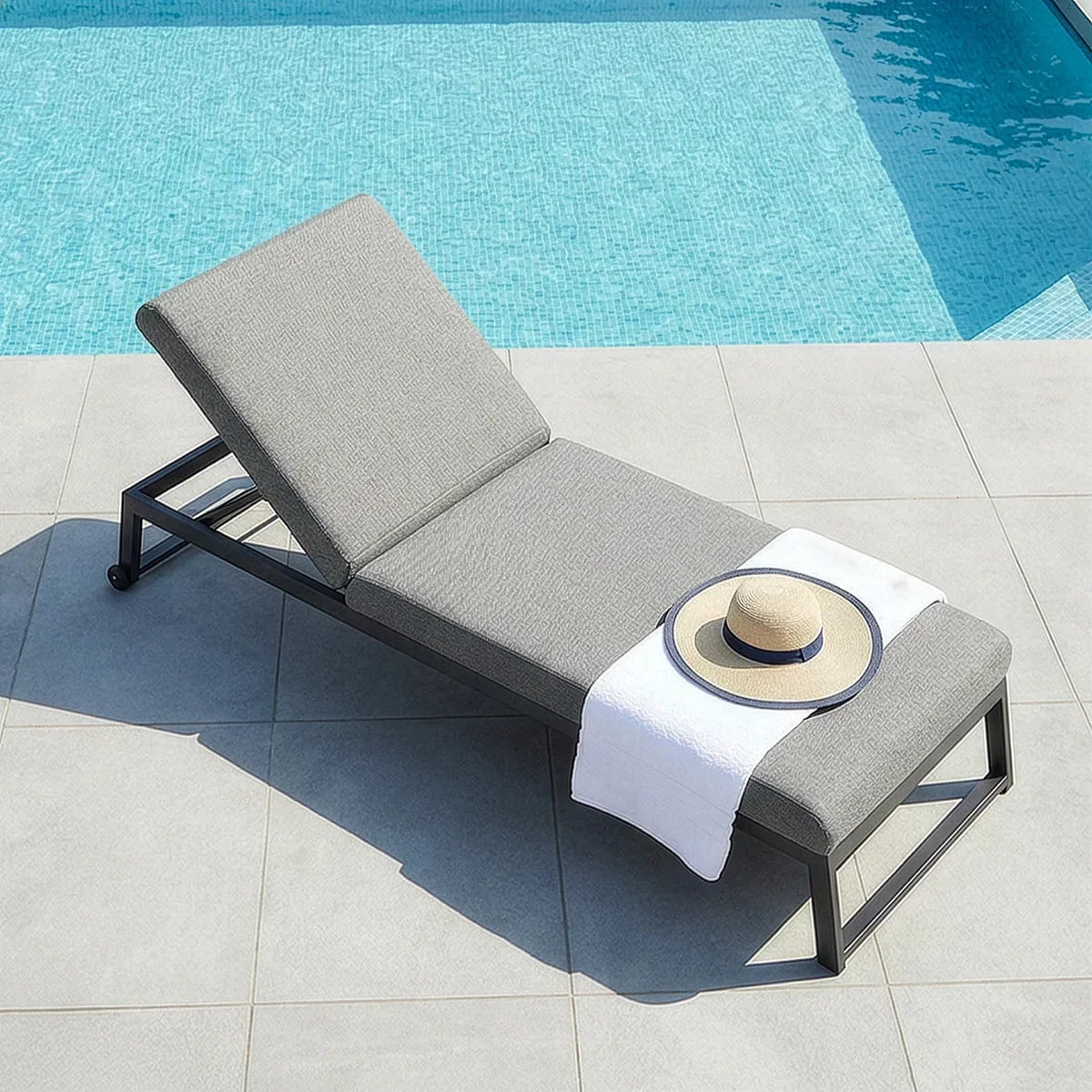 Grey aluminium sun lounger with cushion beside pool, hat and towel on seat